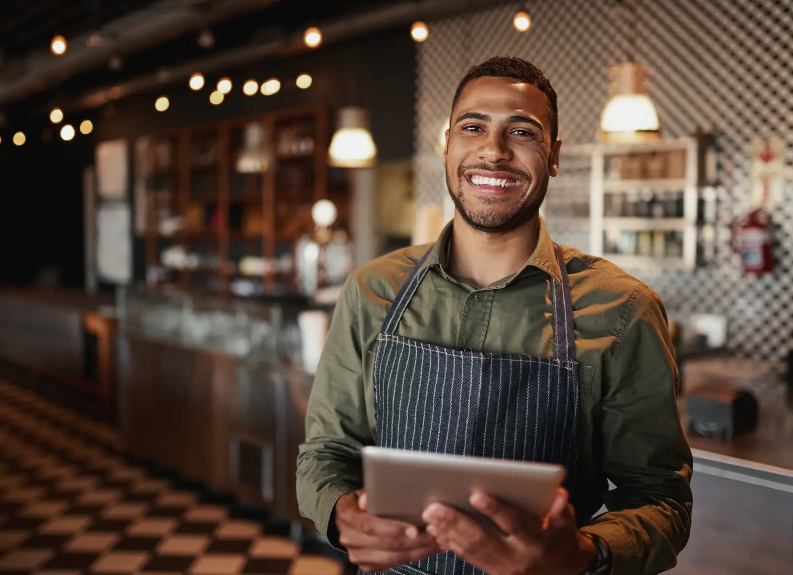 Empreendedor sorrindo com um tablet atrás do balcão do seu café